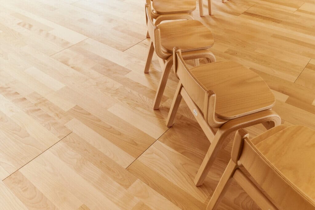 Row of light wooden chairs lined up along a polished wooden floor in a bright room